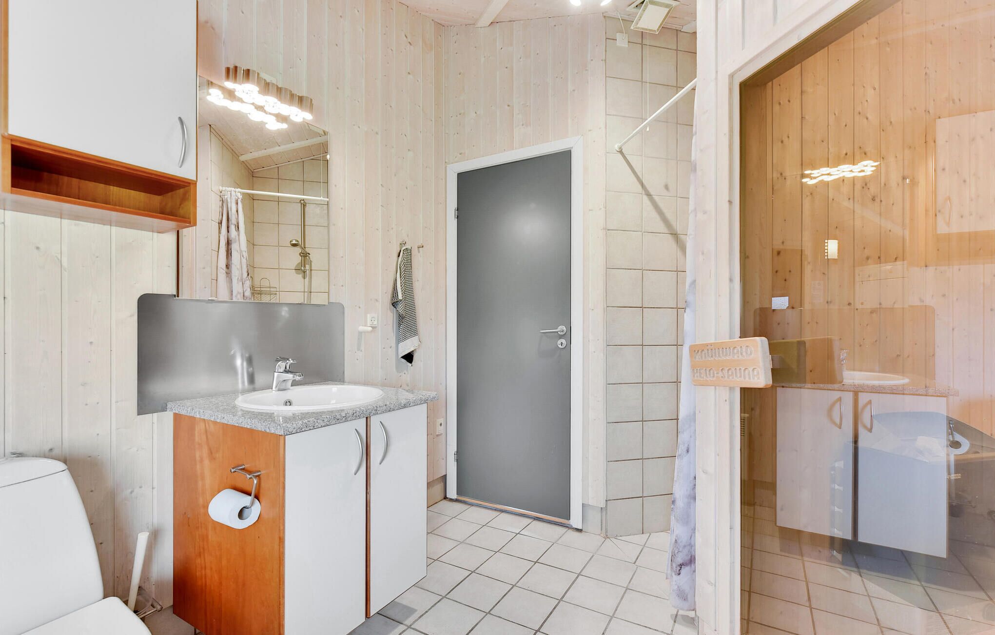 A modern bathroom with a wooden interior, a glass shower enclosure, and a visible sign for a sauna.