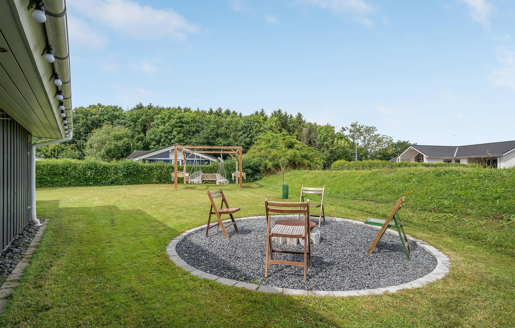 A garden with a wooden swing set, a bench, and a small table surrounded by gravel.