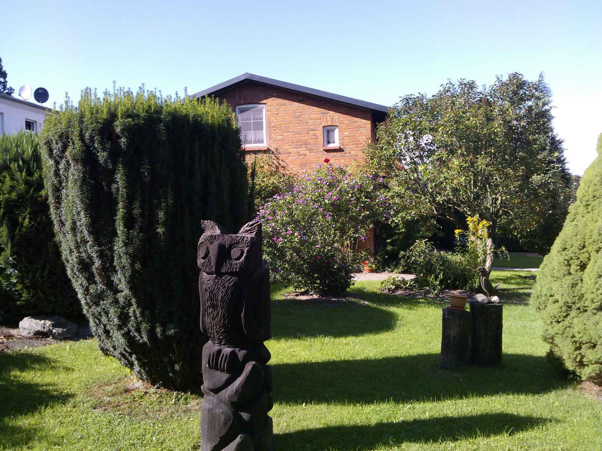 A garden with a sculptural owl, a brick building, and various shrubs and flowers.