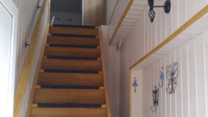 Una escalera de madera con barandilla que conduce a un rellano con una puerta blanca y un aplique de pared.