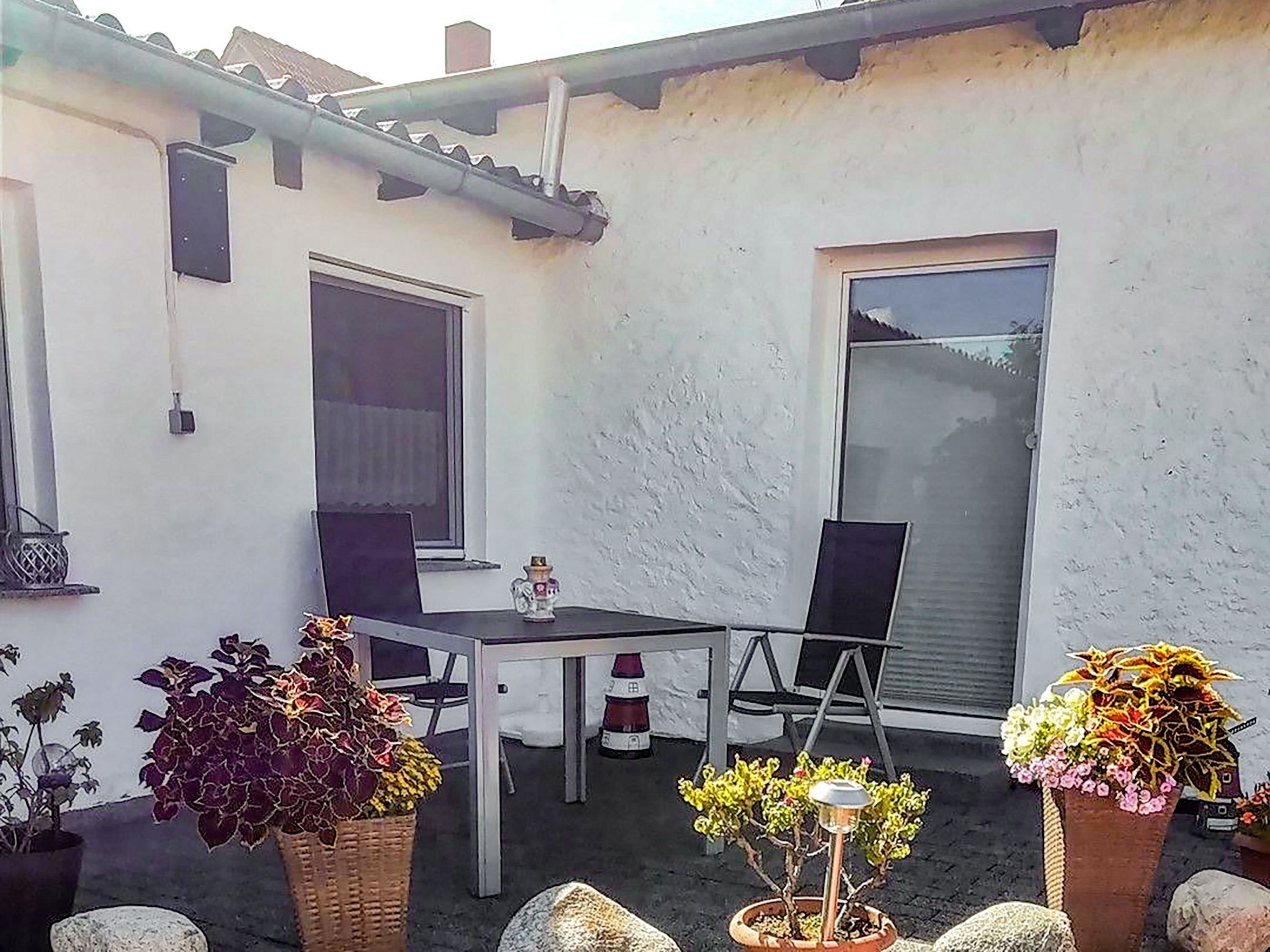 Eine Terrasse mit Tisch, Stühlen und Topfpflanzen, sowie ein Fenster.