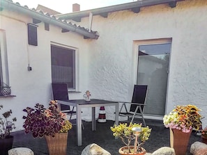 A patio with a table and chairs, potted plants, and a window.