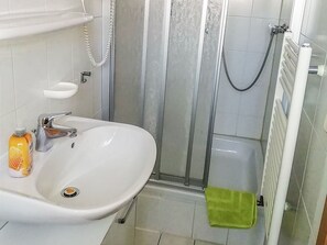 Kylpyhuoneessa on valkoinen pesuallas, käsisuihku ja vihreä pyyhe lattialla.