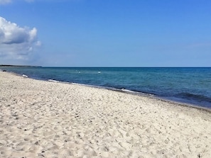 Une plage de sable fin, sous un ciel bleu clair et une mer calme.