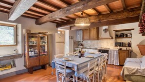 Une cuisine rustique avec des poutres en bois, une table à manger dressée pour quatre personnes et un grand buffet aux portes vitrées.