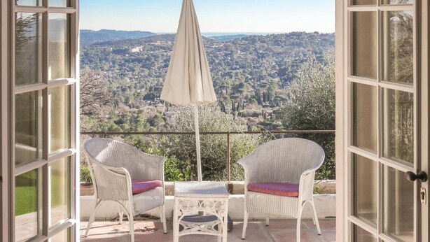Ein offener Balkon mit Korbstühlen und einem Tisch, mit Blick auf eine reizvolle Landschaft.
