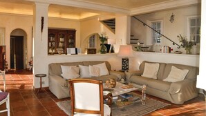 Ein Wohnzimmer mit Sofa, Sessel und Couchtisch, einem Bücherregal und einer Treppe.