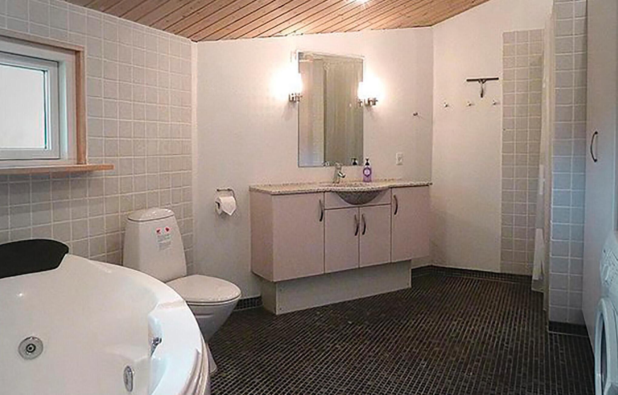 Et badeværelse med toilet, vask med spejl og badekar.