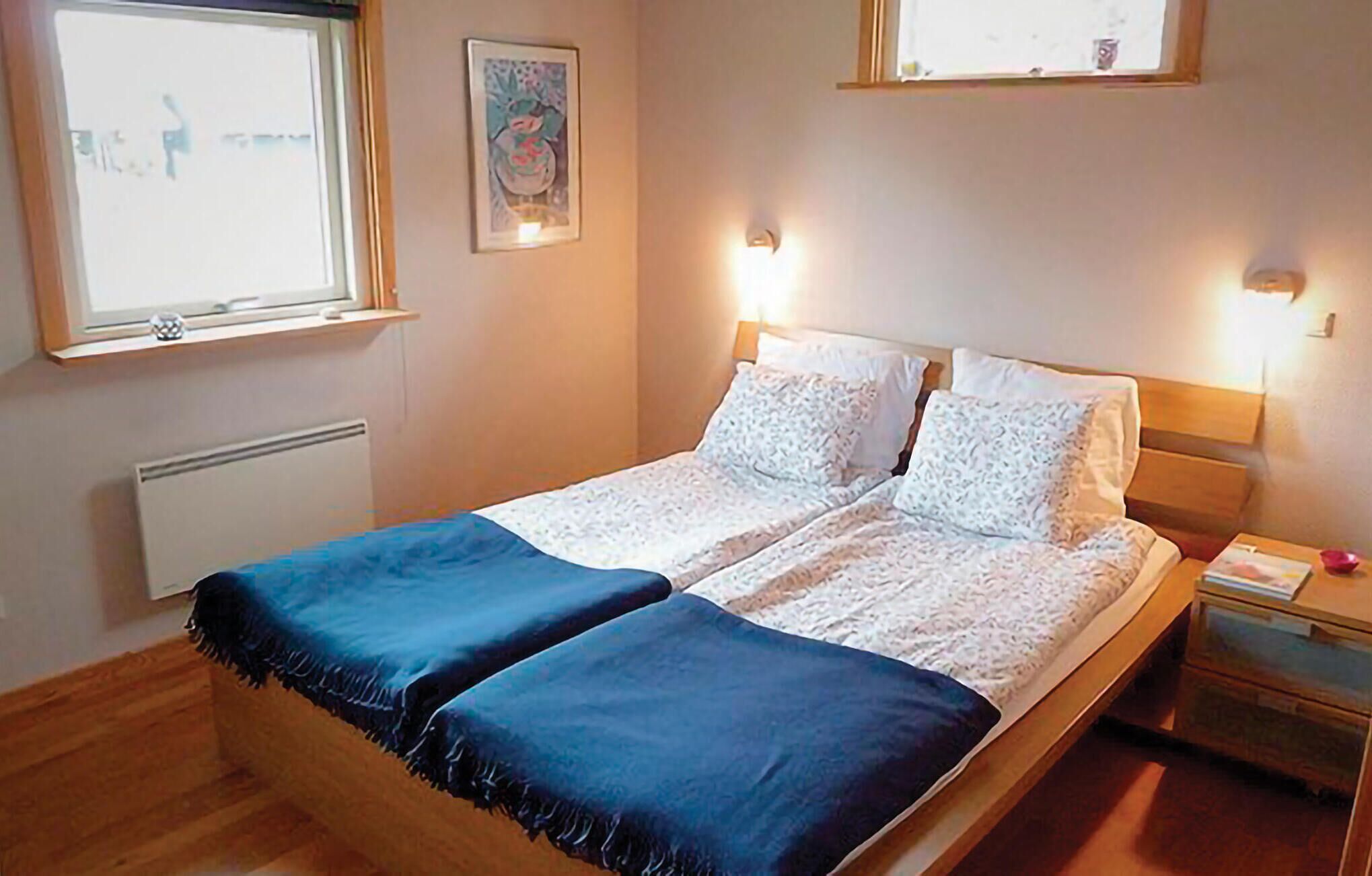 Un lit double avec deux oreillers, une table de chevet avec une lampe et une fenêtre avec des stores.