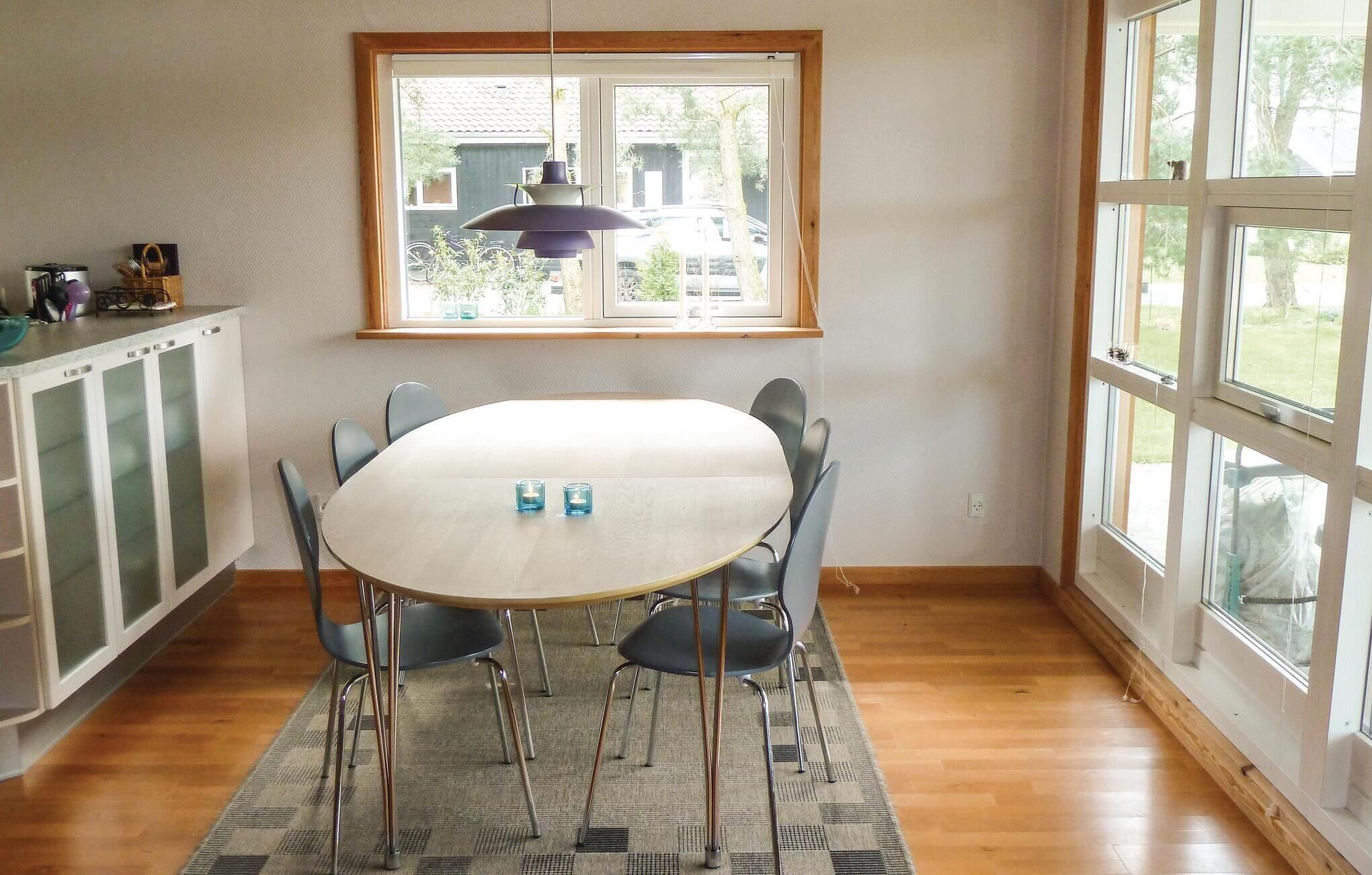A dining area with a round table, four chairs, a hanging light fixture, and a window with a view of the outside.