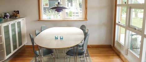 A dining area with a round table, four chairs, a hanging light fixture, and a window with a view of the outside.