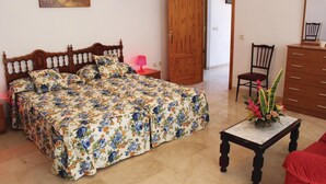 A bedroom with a wooden bed, a nightstand, a dresser, a chair, and a small table with a vase.
