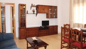 A living room with a blue sofa, wooden cabinets, a TV, and a dining area with wooden chairs and a table.