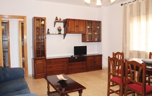 A living room with a blue sofa, wooden cabinets, a TV, and a dining area with wooden chairs and a table.