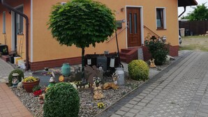 Una casa de dos pisos con techo de tejas, un árbol grande en el frente y un camino de entrada pavimentado.