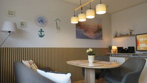 Un comedor moderno con una mesa redonda, dos sillas grises, un jarrón con flores, un reloj y un estante en la pared con objetos decorativos.