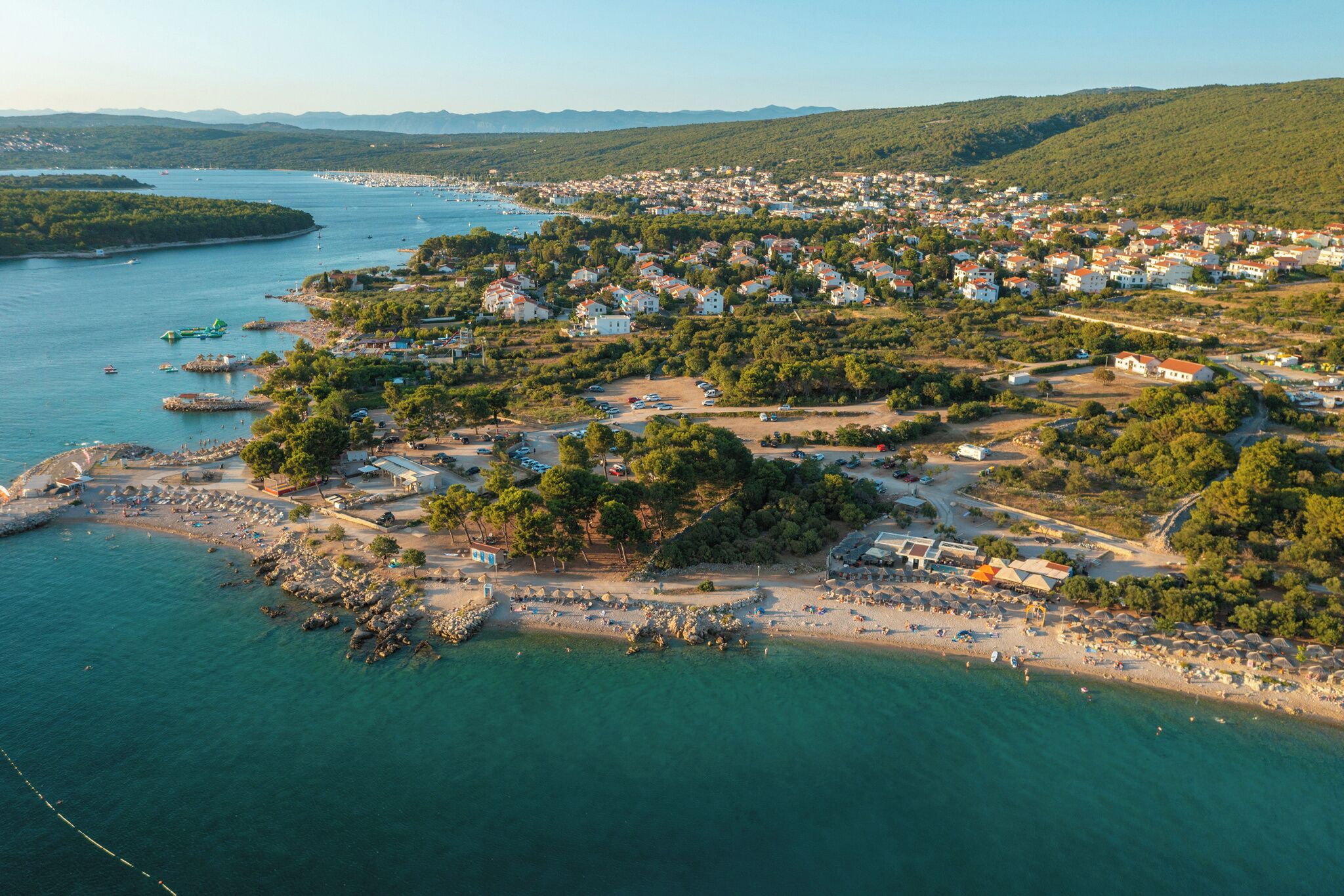 An aerial view of a coastal town with a beach, boats, and residential buildings.