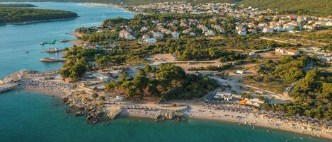 An aerial view of a coastal town with a beach, boats, and residential buildings.