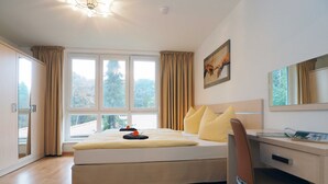 A bedroom with a bed, a desk, and a chair. There are windows with curtains, a painting on the wall, and a ceiling light. - Zempin Ostseepark WE 26 Island Usedom only 150m to the beach - WE 26 (Zempin)