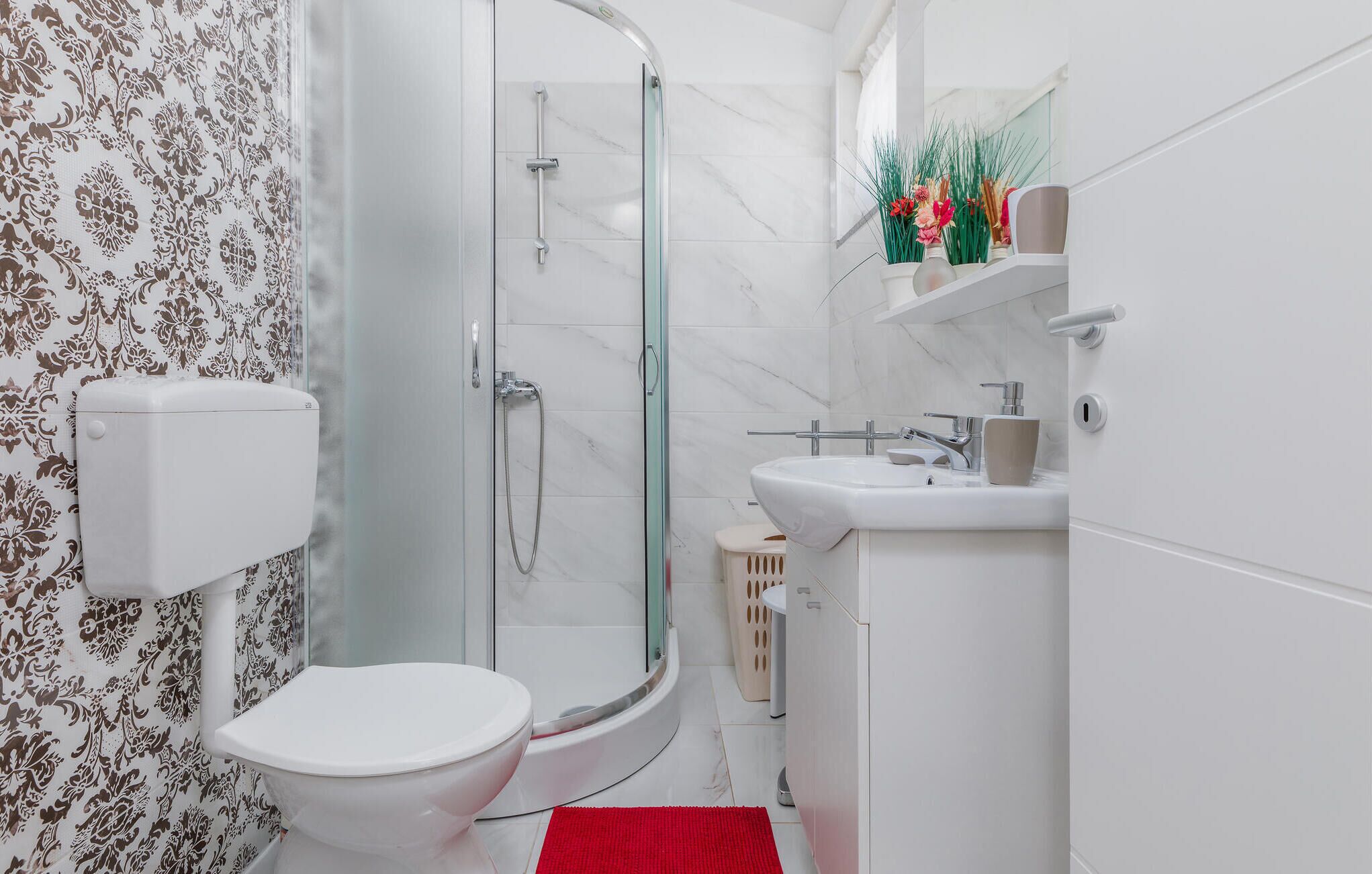 A modern bathroom with a toilet, shower, sink, and a toilet paper holder.