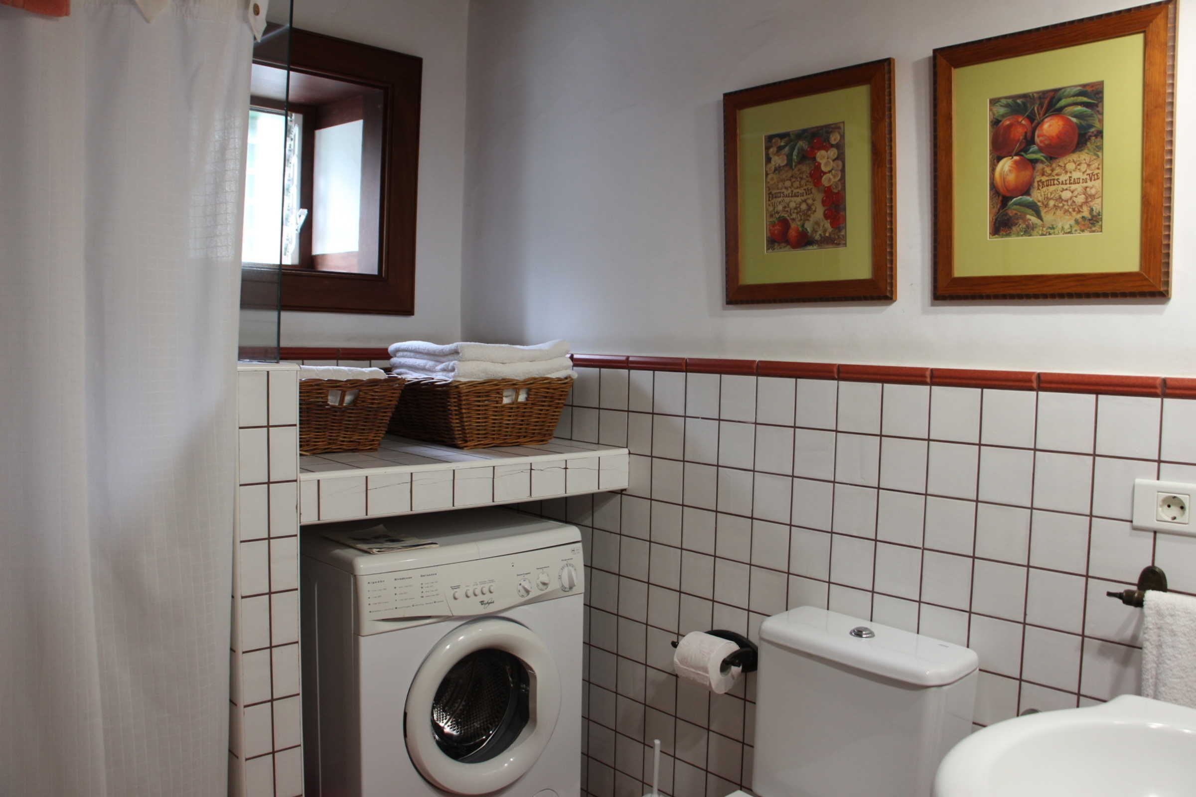 A bathroom with a washing machine, toilet, and two framed pictures on the wall.