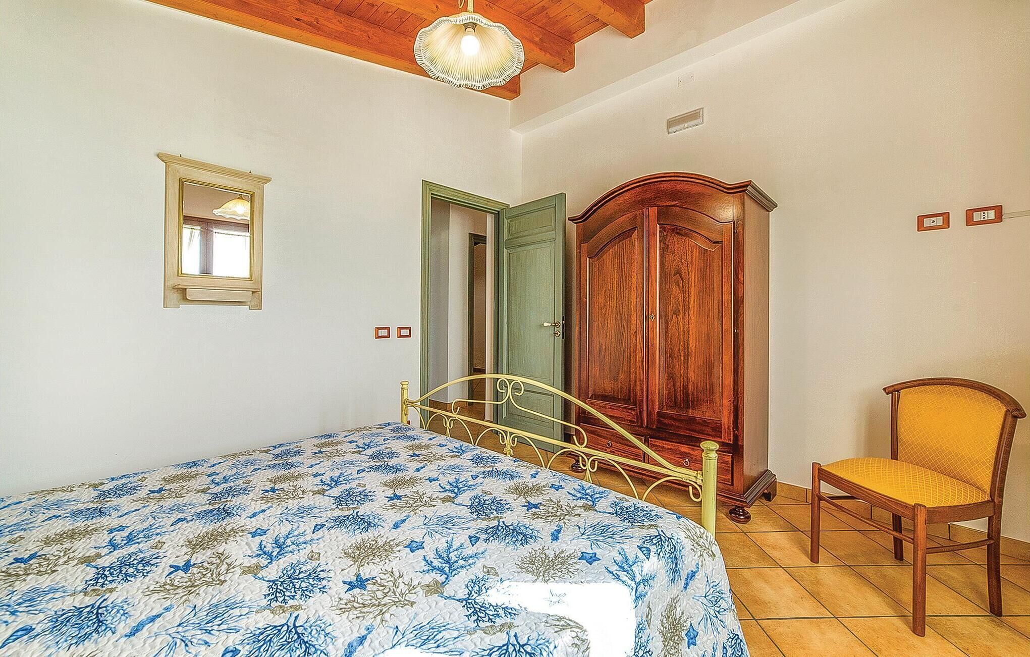 A bedroom with a bed, a wooden wardrobe, a chair, and a mirror.