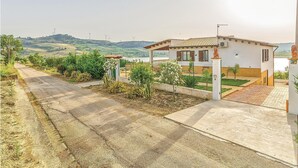 A residential property with a paved driveway, a small garden with various plants, a white building with a tiled roof, and a view of wind turbines in the distance. - Beautiful home in Sambuca di Sicilia AG (Sambuca di Sicilia AG)