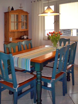 A dining area with a wooden table, blue chairs, a striped tablecloth, a vase with flowers, and a wooden cabinet.