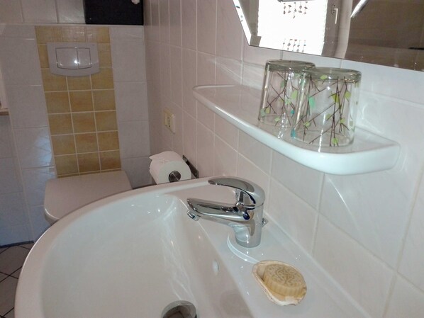 A bathroom with a white sink, a toilet, and a shelf with decorative items.