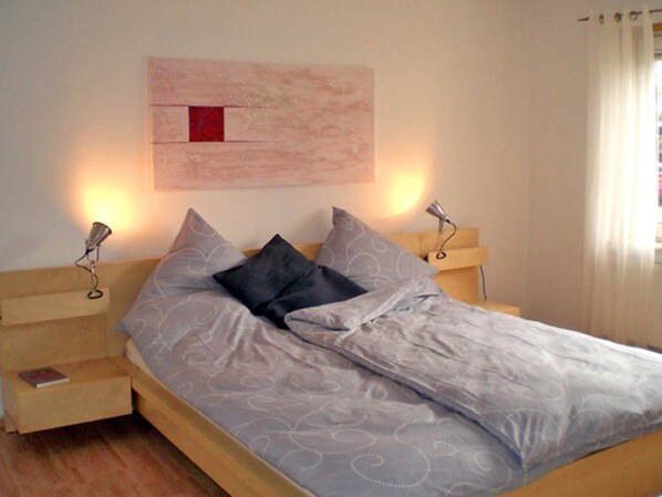 A neatly made bed with a patterned bedspread, two bedside lamps, and a wall-mounted artwork.