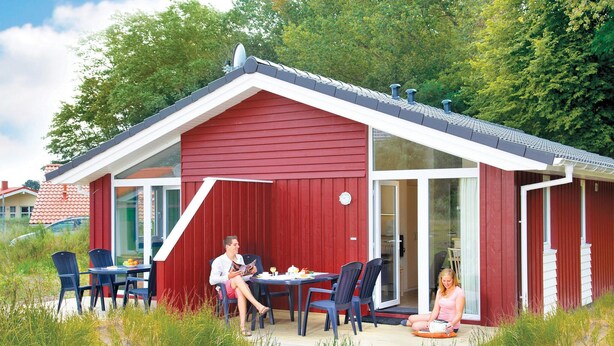 Een rood gebouw met een wit dak, een glazen deur en een terras met stoelen en een tafel.