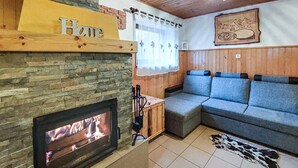 Een gezellige woonkamer met een stenen open haard, een blauwe bank en een houten plafond.