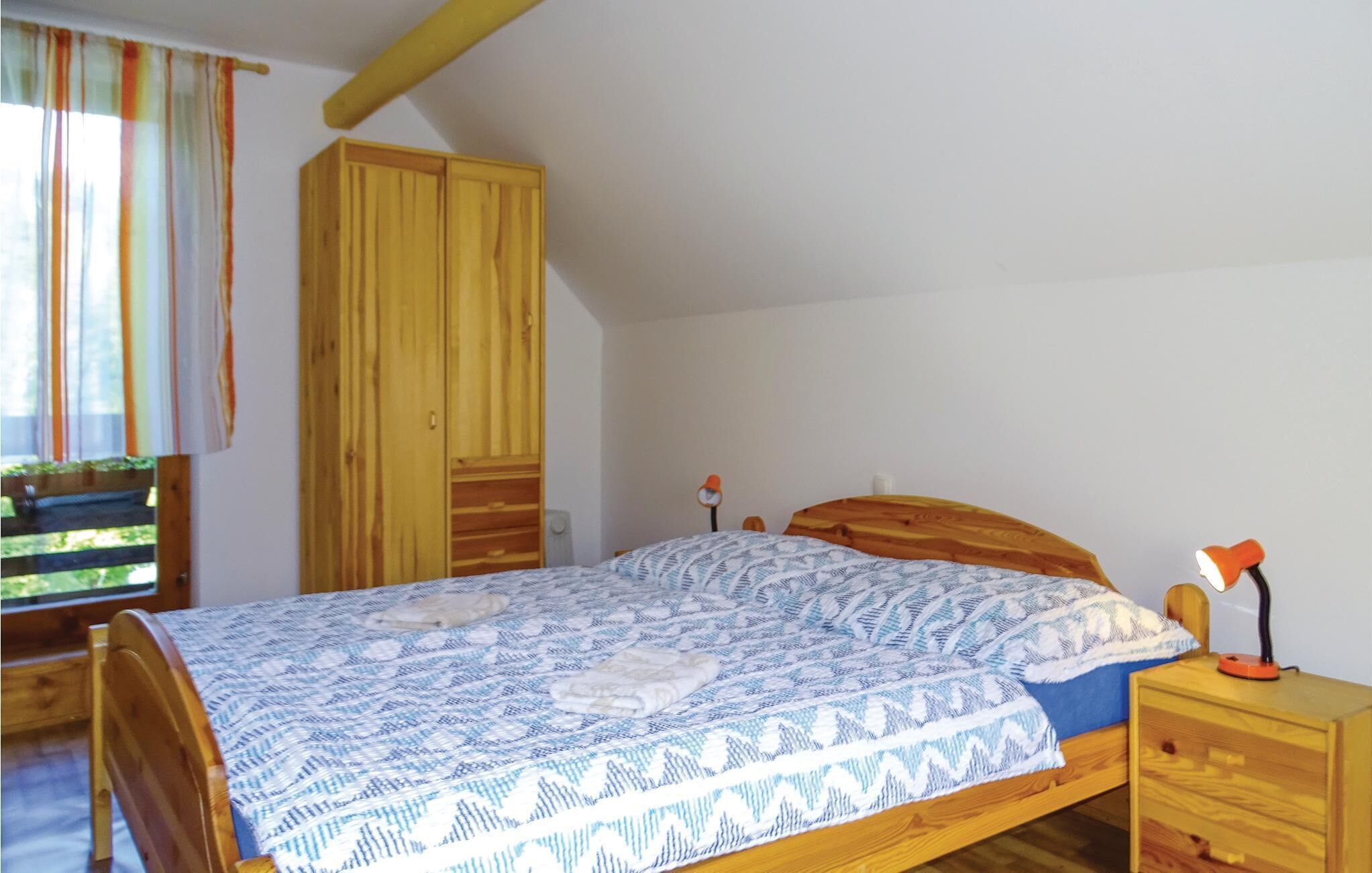 A bedroom with a wooden bed, a nightstand with a lamp, a wardrobe, and a window with curtains.