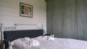 Un letto rifatto con cura, una testiera scura, un quadro appeso sopra e una tenda grigia a destra.