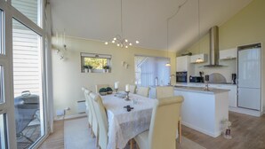 Une cuisine moderne dotée d’un îlot central, d’un coin repas avec une table et des chaises, et d’une grande fenêtre qui laisse entrer la lumière naturelle.