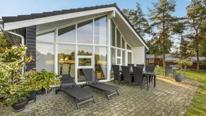 Une maison moderne dotée de grandes fenêtres, d’un patio avec mobilier d’extérieur et d’un jardin.