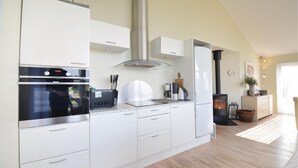 Une cuisine moderne avec des meubles blancs, une hotte en acier inoxydable, un four encastré, une machine à café et un poêle à bois.