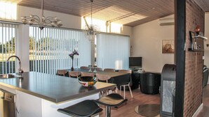 Eine moderne Küche mit Kochinsel, Barhocker, Essbereich mit Tisch und Stühlen, einem Fernseher und einem Kamin.