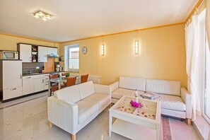 A modern living room with a white sofa, a coffee table with decorative items, and a kitchen area with cabinets and appliances.