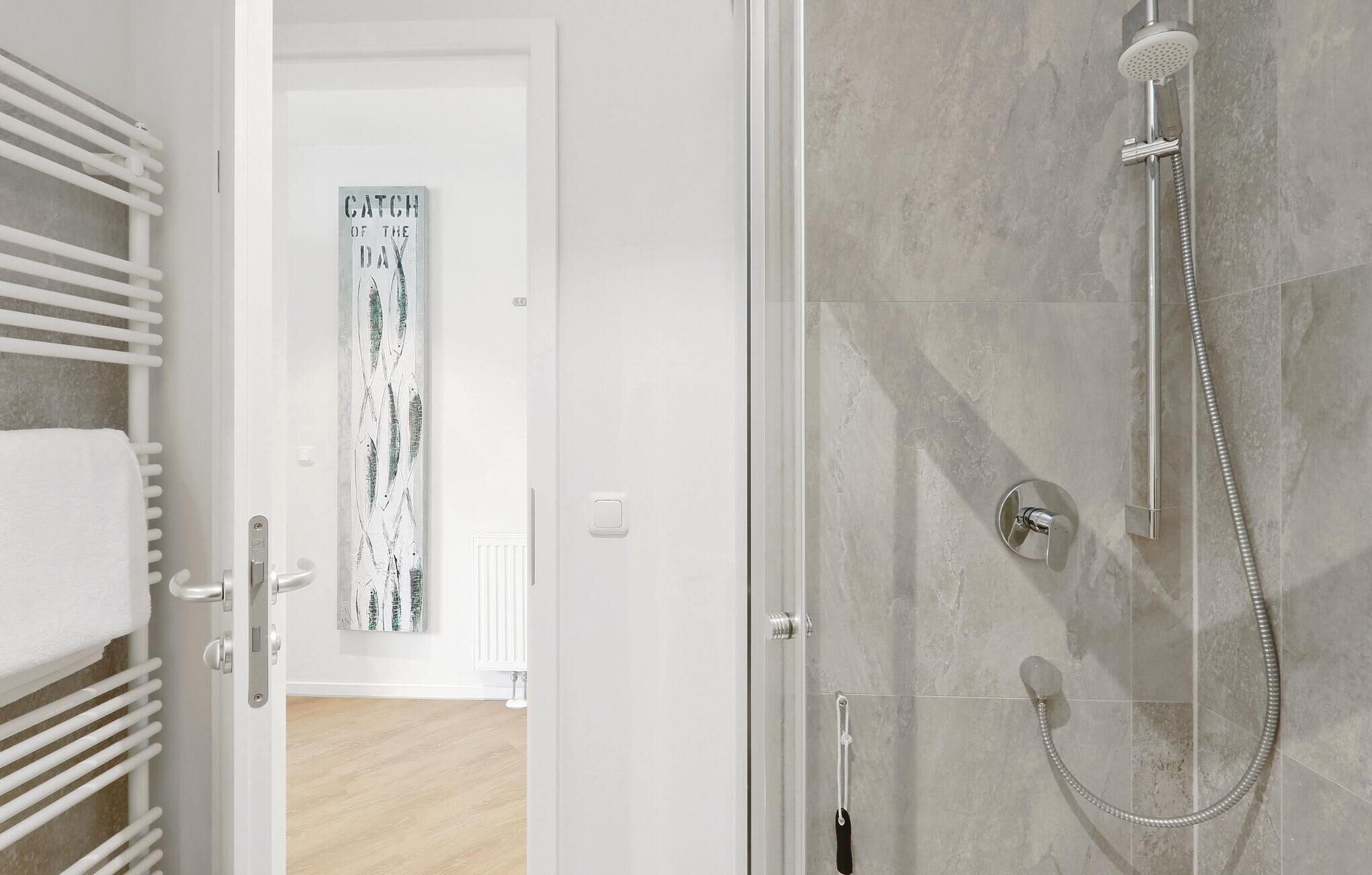 A modern bathroom with a glass shower enclosure, a towel rack, and a door leading to another room.