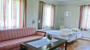 A room with a sofa, a bed, a bedside table with a flower, and curtains.