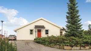 A single-story house with a red door, a small porch, and a gravel driveway.