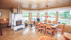 A cozy room with a fireplace, wooden furniture, and large windows offering a view of the outdoors.