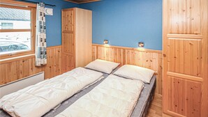 A room with two beds, wooden paneling, a window with curtains, and a radiator.