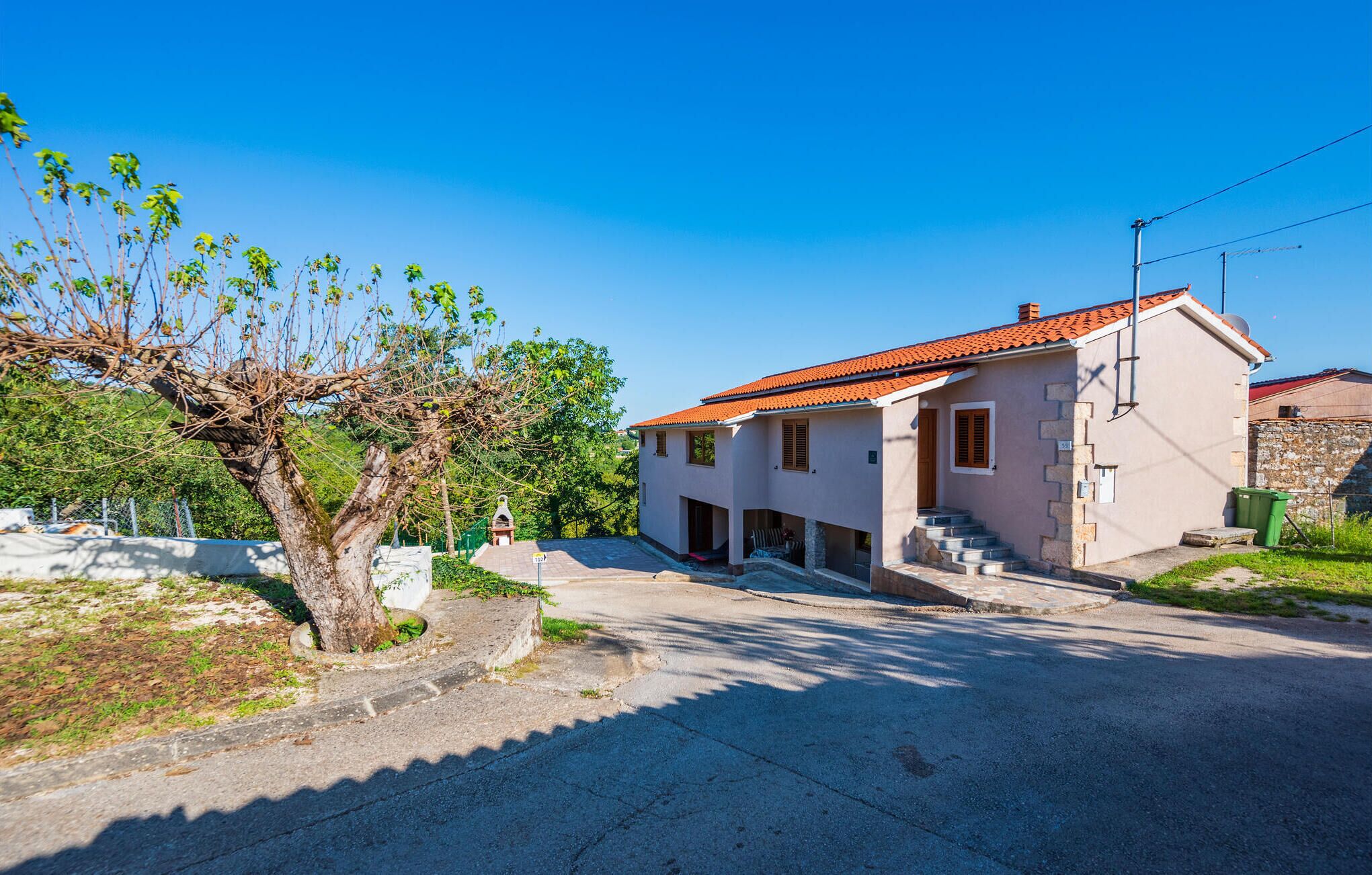 A two-story house with a red-tiled roof, a stone wall, and a small garden area.