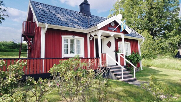 Une maison en bois rouge, avec un toit bleu, des boiseries blanches et un petit porche avec des marches menant à la porte.