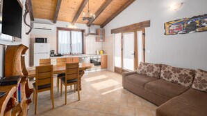 A cozy living room with a brown sofa and a dining area with wooden chairs and a table. - Amazing home in Puzari (Puzari)