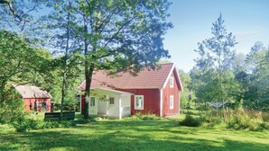Ein rotes Holzhaus mit geneigtem Dach, umgeben von üppigem Grün und Bäumen.