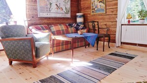 Ein gemütlicher Raum mit Holzwänden, einem karierten Sofa, einem Holzschaukelstuhl und einem Tisch mit blauer Tischdecke.