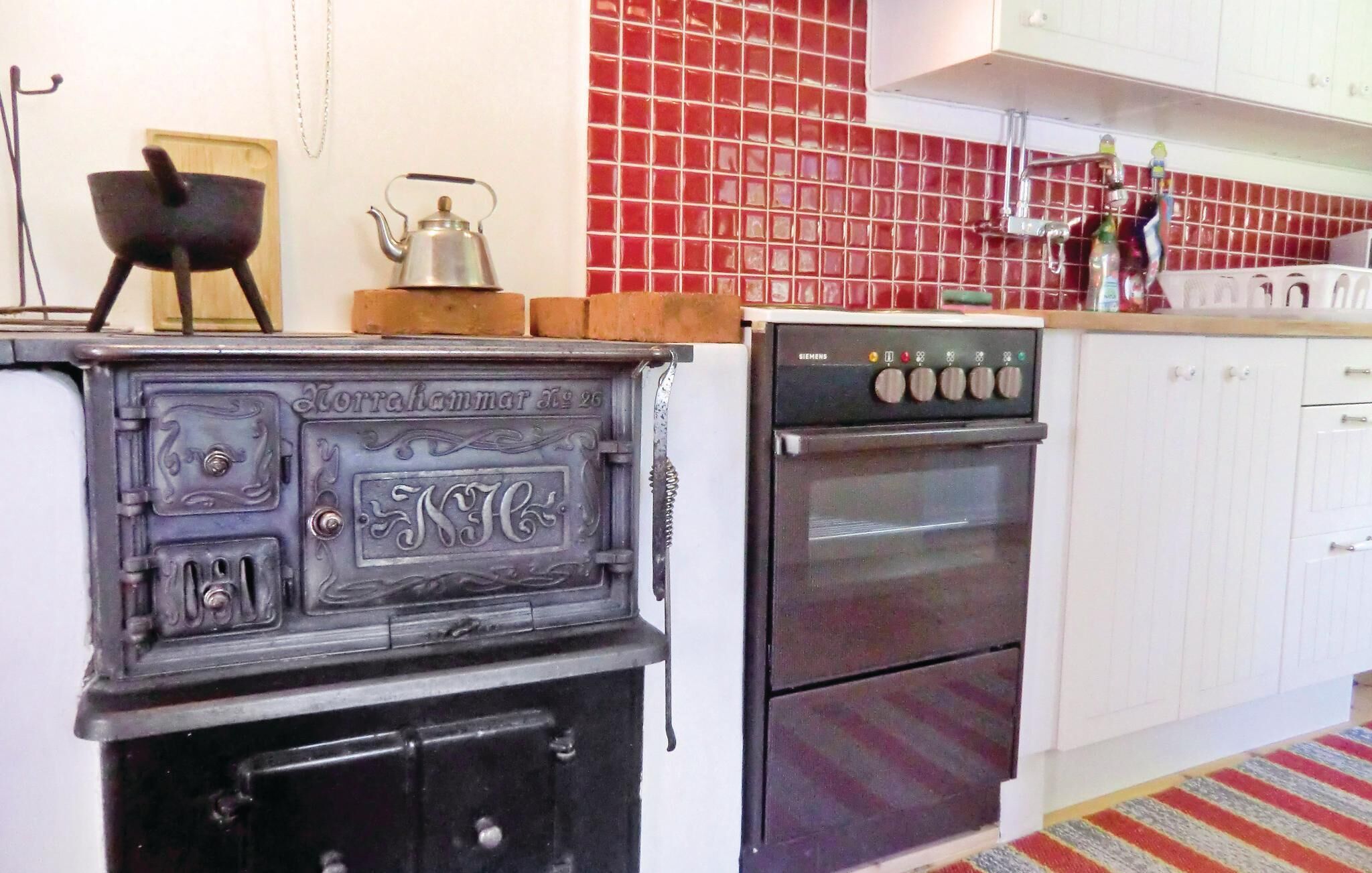 A kitchen with a vintage stove, a Siemens oven, and red tiled backsplash.